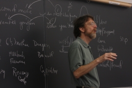 professor Craig Williamson stands in front of a blackboard